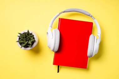 Ses kitabı konsepti. Kulaklıklar, kitap ve yeşil bitki sarı arka planda. Düz yatıyordu.