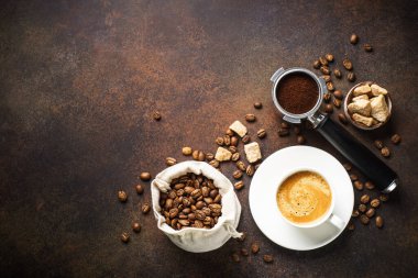 Bir fincan kahve, kavrulmuş kahve çekirdekleri ve koyu masada filtre tutacağı. Kopyalama alanı olan üst görünüm.