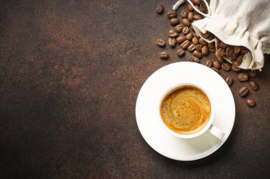 Koyu masada bir fincan kahve ve kavrulmuş kahve çekirdeği. Tasarım için alanı olan üst görünüm.