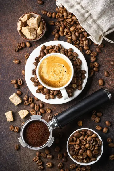 Bir fincan kahve, kavrulmuş kahve çekirdekleri ve koyu masada filtre tutacağı. Üst görünüm, kapat, dikey görüntü.