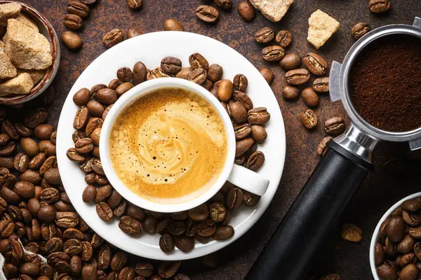 Bir fincan kahve, kavrulmuş kahve çekirdekleri ve koyu masada filtre tutacağı. Üst görünüm, kapat.