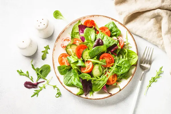 Salad from green leaves and vegetables. Fresh green salad in white plate. Top view.
