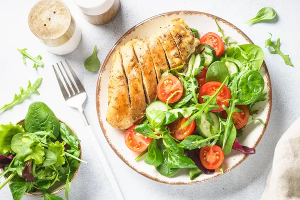 Green salad with chicken fillet on white. Diet food, healthy nutrition. Top view with copy space.