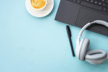 Dizüstü bilgisayarı, kulaklığı, not defteri ve kahve fincanı olan ofis alanı. Fotokopi alanı ile mavi üzerine düz resim yatıyordu.