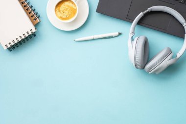 Office table desk with laptop, notepad, pen and cup of coffee. Flat lay on blue with copy space.