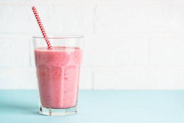 Mavi arka planda uzun bardakta çilekli smoothie ya da milkshake..