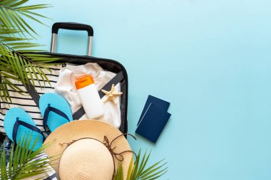 Üzerinde yazlık kumaş, ayakkabı ve aksesuarlar olan bavulu mavi arka planda aç. Yaz tatilleri, seyahat konsepti. Düz görünüm.