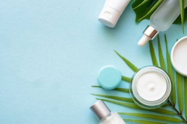 Doğal kozmetik ürünleri. Krema, serum, yeşil tropikal yapraklı tonik. Dizayn için alanı olan mavi arkaplan üzerinde düz uzandı.