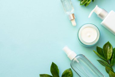 Doğal kozmetik ürünleri. Krema, serum, yeşil tropikal yapraklı tonik. Dizayn için alanı olan mavi arkaplan üzerinde düz uzandı.