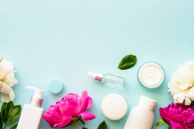 Doğal kozmetik ürünleri. Krema, serum, yeşil yapraklı ve çiçekli tonik. Mavi arka planda düz uzandı.