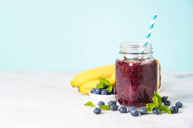 Mavi arka planda cam kavanozda yabanmersini muzlu smoothie..