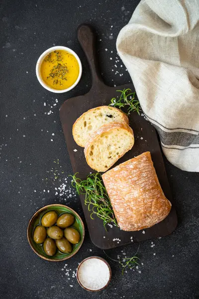 Tahtada ciabatta ekmeği, zeytin yağı, zeytin ve bitkilerle birlikte. Siyah üzerine kopyalama alanı olan üst görünüm.