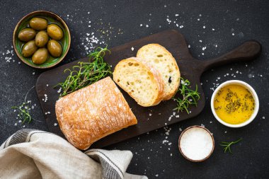 Ciabatta ekmeği, zeytinyağı, zeytin ve biberiye ile siyah masada. Akdeniz yemekleri. Üst görünüm.