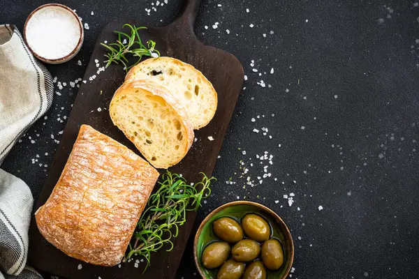 Tahtada ciabatta ekmeği, zeytin yağı, zeytin yağı ve siyah otlar. Kopyalama alanı olan üst görünüm.