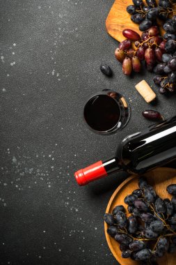 Kırmızı şarap siyah arka planda. Bir bardak şarap, şişe, çatal bıçak ve tirbuşon. Düz, dikey.