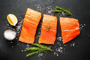 Baharatlı, biberiyeli ve limonlu taze somon filetosu. Siyah arkaplanda üst görünüm.