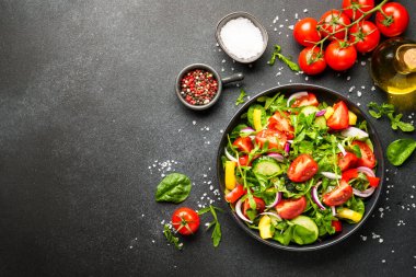 Siyah arka planda sağlıklı yiyecekler. Yapraklı salata, domates, biber ve zeytinyağı..
