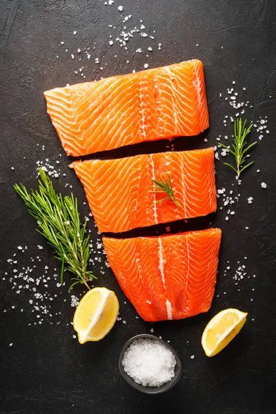 Baharatlı, biberiyeli ve limonlu taze somon filetosu. Siyah arkaplanda üst görünüm.