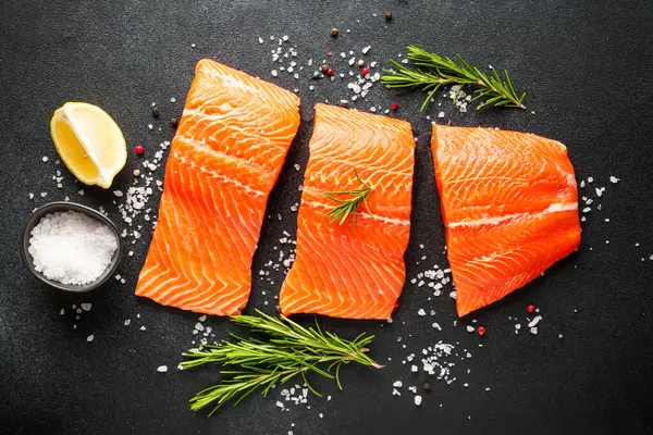 Baharatlı, biberiyeli ve limonlu taze somon filetosu. Siyah arkaplanda üst görünüm.