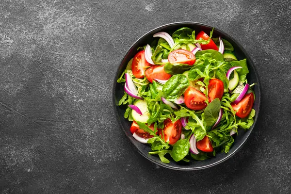 Yapraklı ve sebzeli taze salata. Siyah üzerine üst görünüm.