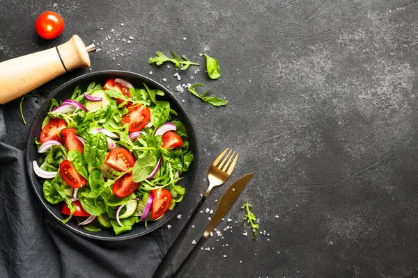 Yapraklı ve sebzeli taze salata. Siyah üzerine üst görünüm.