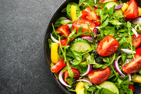 Yapraklı taze salata, domates, biber ve siyah arka planda zeytinyağı. Üst görünüm, makro.