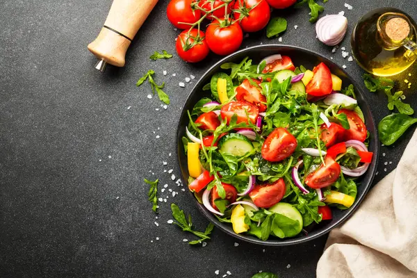 Siyah arka planda sağlıklı yiyecekler. Yapraklı salata, domates, biber ve zeytinyağı..