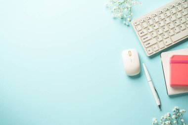 Klavyeli, defterli, mavi arka planda kalem ve çiçekli bir işyeri. Kopyalama alanı olan üst görünüm.
