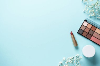 Makyaj ürünleri mavinin üzerine seriliydi. Kozmetik palet, fırçalar, rujlar ve beyaz çiçekler..