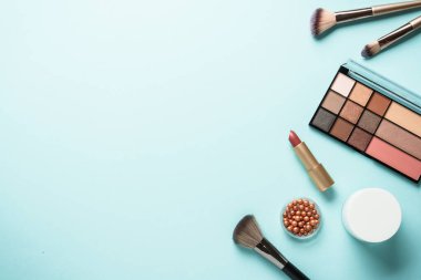 Makyaj paleti, fırçalar ve mavi arka planda ruj. Tasarım için alanı olan üst görünüm.