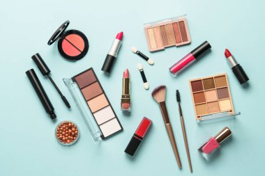 Mavi arka plandaki ürünleri düzleştirin. Kozmetik palet, fırça, krem ve ruj.