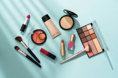 Mavi arka planda sert gölgeli ürünler uydur. Kozmetik palet, fırçalar ve ruj.