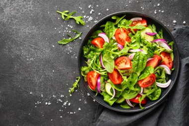 Yapraklı ve sebzeli taze salata. Siyah arkaplanda tasarım için alanı olan üst görünüm.