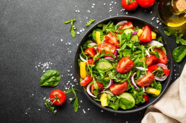 Siyah arka planda sağlıklı yiyecekler. Yapraklı salata, domates, biber ve zeytinyağı..