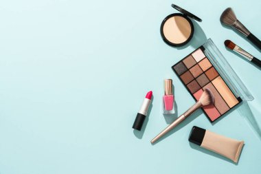 Mavi arka plandaki ürünleri düzleştirin. Kozmetik palet, fırça, krem ve ruj.