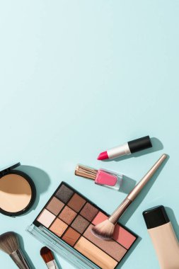 Mavi arka plandaki ürünleri uydur. Kozmetik palet, fırçalar, krem ve ruj. Kopyalama alanı olan düz resim