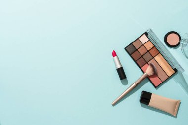 Mavi arka plandaki ürünleri uydur. Kozmetik palet, fırçalar, krem ve ruj. Kopyalama alanı olan düz resim