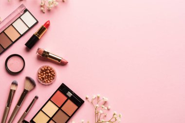 Makyaj ürünleri ve çiçekler pembe arka planda. Göz farı, fosforlu kalem, krem, ruj ve kozmetik fırçalar..