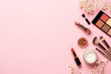 Makyaj ürünleri ve çiçekler pembe arka planda. Göz farı, fosforlu kalem, krem, ruj ve kozmetik fırçalar..