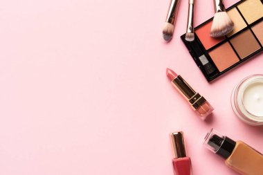 Makyaj ürünleri pembeye yatar. Göz farı, fosforlu kalem, krem, ruj ve kozmetik fırçalar..
