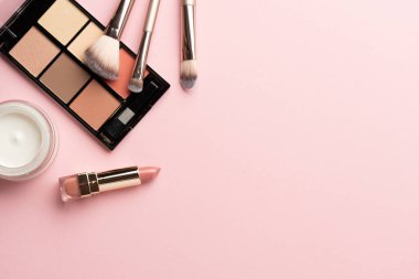 Makyaj ürünleri pembeye yatar. Göz farı, fosforlu kalem, krem, ruj ve kozmetik fırçalar..