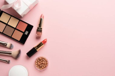 Göz farı paleti, fosforlu kalem, krem, ruj ve kozmetik fırçalar. Pembe arka planda düz uzandı.