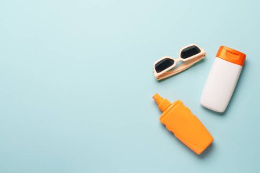 Mavi arka planda güneş kremi ve güneş gözlüğü. Kopyalama alanı olan düz.