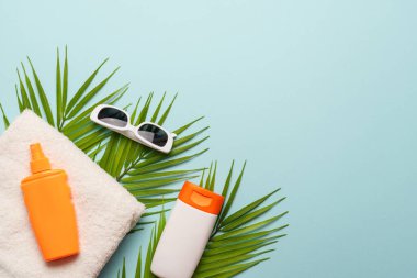 Mavi arka planda güneş kremi, havlu ve güneş gözlüğü. Kopyalama alanı olan düz.