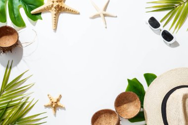 Palmiye yaprakları, şapka, güneş gözlükleri, beyaz arka planda deniz kabukları, güneşli gölgeler. Düz görünüm.