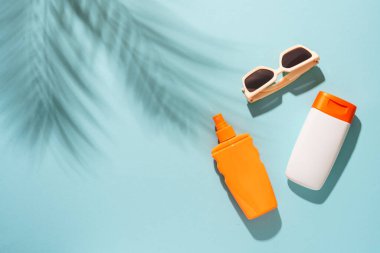 Mavi arka planda güneş kremi ve güneş gözlüğü ve sert, güneşli gölgeler. Güneş koruması.