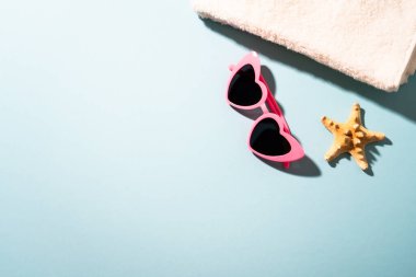 Yaz düzlüğü arka plandaydı. Güneş gözlüğü, beyaz havlu ve güneşli gölgeli deniz kabuğu..