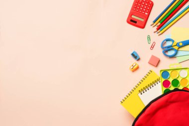 Renkli arka planda kırtasiye malzemesi olan okul çantası. Kopyalama alanı olan düz