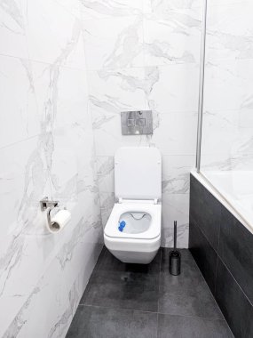 Dahili su tankı sistemi olan modern bir klozet. Duvarlarda beyaz mermer fayanslar ve modern gri zemin.