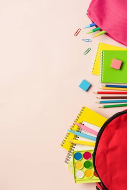 Okula dönelim. Renkli arka planda kırtasiye malzemesi olan okul çantası. Düz konum, dikey biçim.